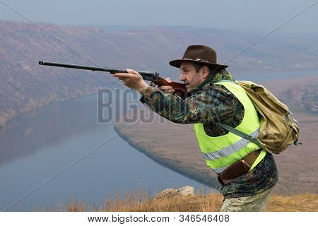 Hunter Man In Camouflage With A Gun During The Hunt In Search Of Wild Birds Or Game. Autumn Hunting 