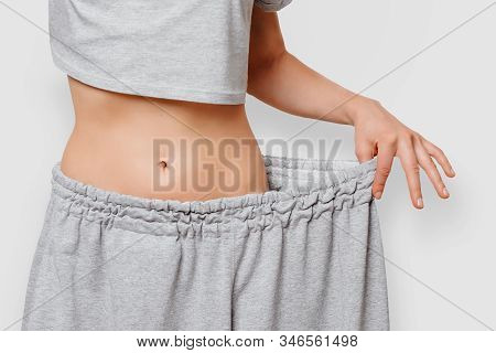 Close-up Of Slim Waist Of Young Woman In Big Pants Showing Successful Weight Loss, Isolated On White
