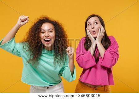 Two Funny Women Friends European African American Girls In Pink Green Clothes Posing Isolated On Yel