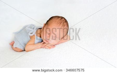 Newborn beatiful cute baby sleeping curled up in white blanket on white bed background