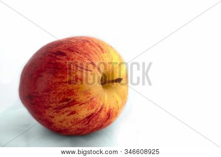 An Organic Red And Yellow Apple Lays On Its Side, Stem Toward Camera On A White Background