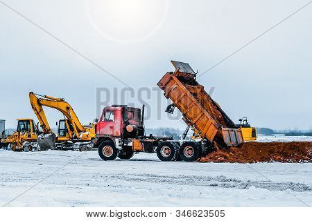 Dump Truck Is Moving Down Sand On Construction Site. Leveling The Ground. Signalman On Construction 