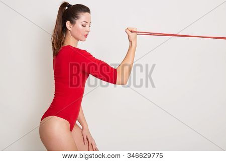 Horizontal Shot Of Young Beautiful Woman Working Out With Straps, Tarining Biceps, Wearing Red Styli