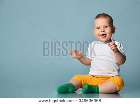 Frolic Infant Child Baby Boy Kid In Yellow Pants And White T-shirt Is Sitting On The Floor Stick His