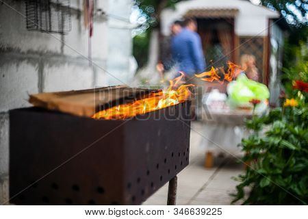 B-b-q Outdoors Background. Kindling Wood Barbecue Outdoors With Open Flame Against The Background Of