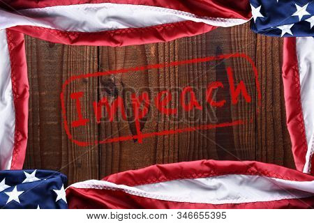 Top view of an American flags on a dark wood table forming a frame with the word Impeach in the middle.
