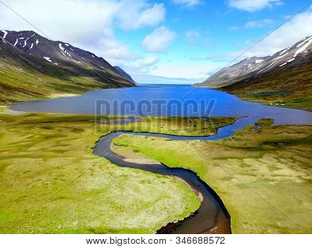 The Aerial View Of A Blue Creek Flowing Into The Lake Near Hedinsfjordur, Iceland