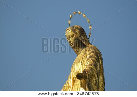 Close Up View Of The Golden Madonnina (madonna - Immacolata) Statue Against The Blue Sky Located At 