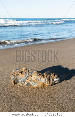 closeup of a used plastic bottle, covered with wet sand, on the sand of a lonely beach, brought back by the ocean to the seashore