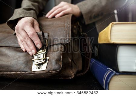 Hand Fastens A Buckle On An Old Brown, Classic, Leather Briefcase, Which Stands On A Table, Next To 