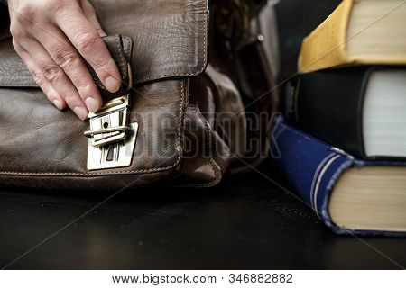 Hand Fastens A Buckle On An Old Brown, Leather Briefcase, Which Stands On A Table Next To Books.