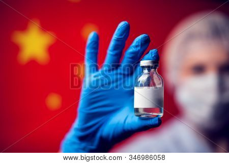 A Doctor In Blue Medical Gloves And Mask Holding An Ampula With Vaccine In Front Of Flag Of China. C