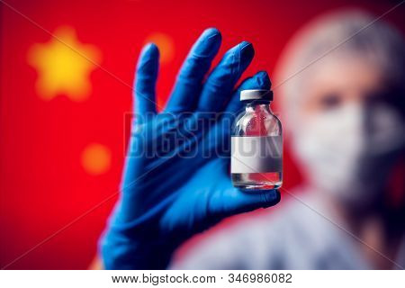 A Doctor In Blue Medical Gloves And Mask Holding An Ampula With Vaccine In Front Of Flag Of China. C