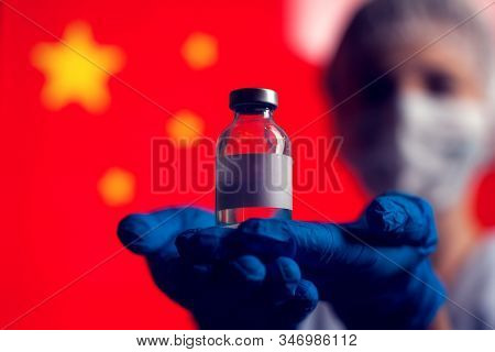 A Doctor In Blue Medical Gloves And Mask Holding An Ampula With Vaccine In Front Of Flag Of China. C