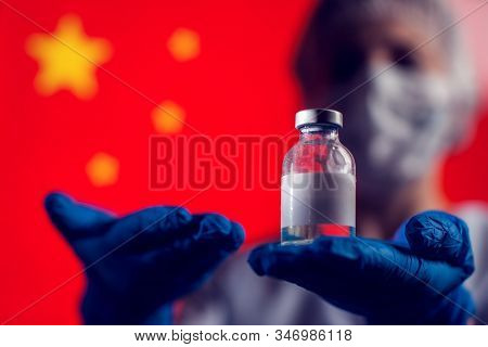 A Doctor In Blue Medical Gloves And Mask Holding An Ampula With Vaccine In Front Of Flag Of China. C