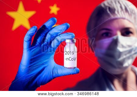 A Doctor In Blue Medical Gloves And Mask Holding An Ampula With Vaccine In Front Of Flag Of China. C