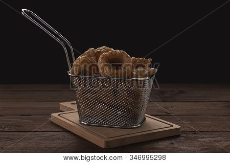 Horizontal View On Foreground Of Some Pork Rinds In A Small Metal Basket On A Stand And Wooden Table