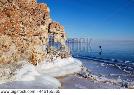 A Lonely Girl Is Skating On The Transparent Ice Of The Frozen Lake Baikal. Winter Travel In Russia.