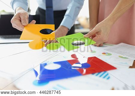 Close-up Of Businessman And Businesswoman Colleagues Solving Jigsaw Puzzle On Desk. Put Colourful Pu