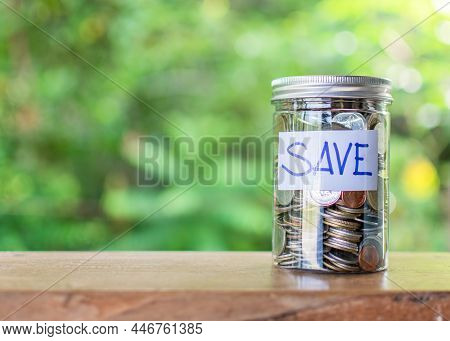 Blurred Background, Coins And Text Save In A Glass Jar Placed On A Wooden Table. Concept Of Saving M