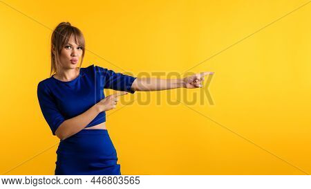 Funny Girl Pointing Index Finger Aside On The Right And Looking At Camera On Yellow Background. Youn