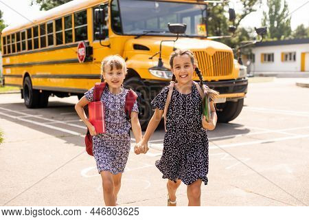 Cheerful Little Girls Next To School Bus. Backback. Back To School Concept.