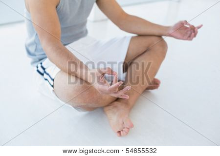 Close-up low section of a young man sitting in lotus pose on the floor