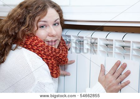 Young Woman Leaning To Central Heating Convector For Warming Hands