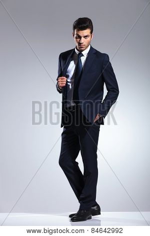 Full length picture of a handsome young business man pulling his jacket while holding one hand in his pocket.