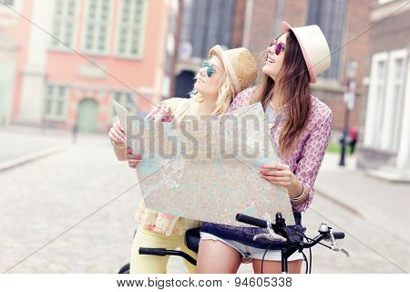 A picture of two girl friends using a map and riding a tandem bicycle in the city