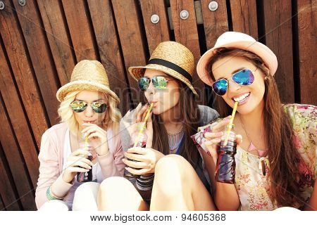 A picture of a group of girl friends drinking soda on the pier