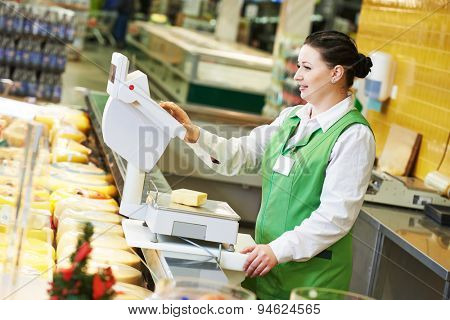 seller woman assistant in supermarket working with scales balance weghing cheese at shop