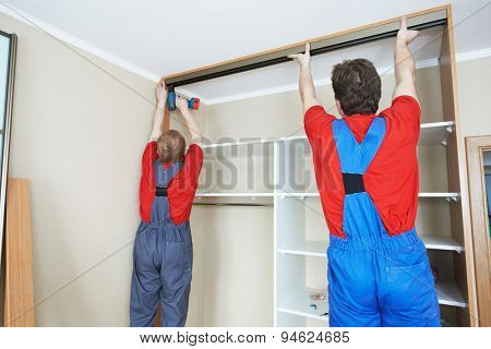 Two carpenters workers joint and settle home built-in cupboard