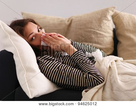 Portrait of a sick woman blowing her nose while sitting on the sofa