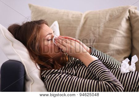 Portrait of a sick woman blowing her nose while sitting on the sofa