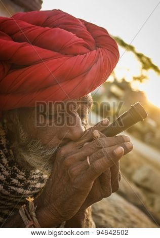 GODWAR REGION, INDIA - 14 FEBRUARY 2015: Elderly Rabari tribesman with red turban and blanket smokes chillum. Rabari or Rewari are an Indian community in the state of Gujarat.