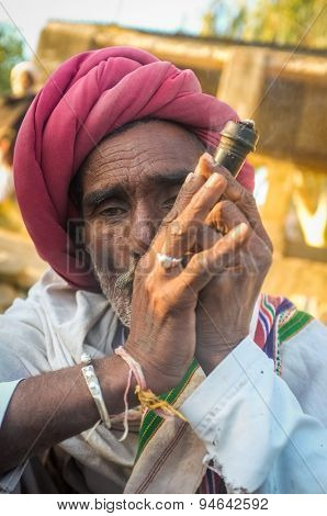 GODWAR REGION, INDIA - 14 FEBRUARY 2015: Elderly Rabari tribesman with red turban and blanket smokes chillum. Rabari or Rewari are an Indian community in the state of Gujarat.
