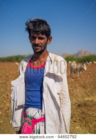 GODWAR REGION, INDIA - 14 FEBRUARY 2015: Young Rabari shepherd with no turban stands in field with cattle. Rabari are an Indian community in the state of Gujarat.