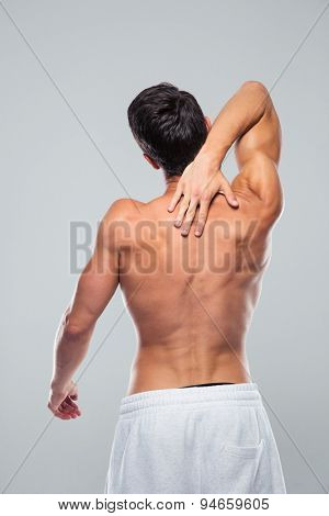 Rear view portrait of a muscular man with neck pain over gray background