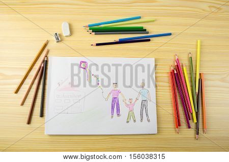 Shot of a drawing with painting supplies and pencils on a wooden table with a picture of a gay couple with their daughter