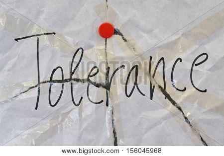 Word Tolerance written on torn background with red pin