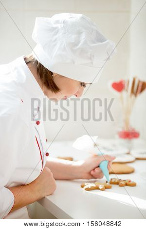 Professional female confectioner bent decorating a gingerman with icing sugar using a pastry bag, preparing for Christmas. Lifestyle, vertical, Christmas concept photo