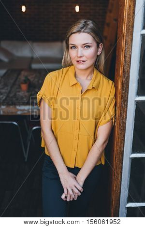 Portrait of an attractive young blonde woman smiling while standing at the door to her modern loft apartment