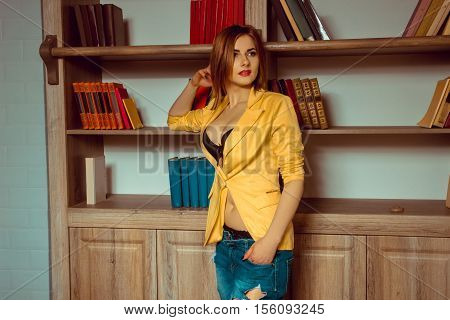 lovely young girl in a yellow jacket unbuttoned posing against the backdrop of a bookcase