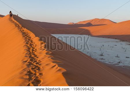 Walking on the Sand dunes at Sossusvlei in Southern Namibia at sunrise above a white salt pan