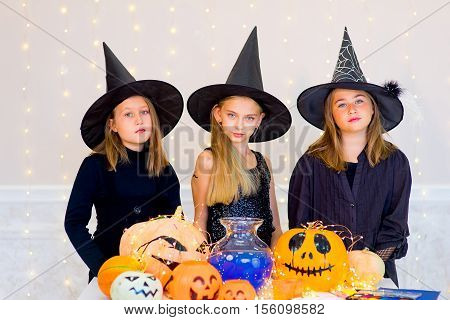 Happy group of teenagers in costumes during Halloween party playing around the table with pumpkins and bottle of potion