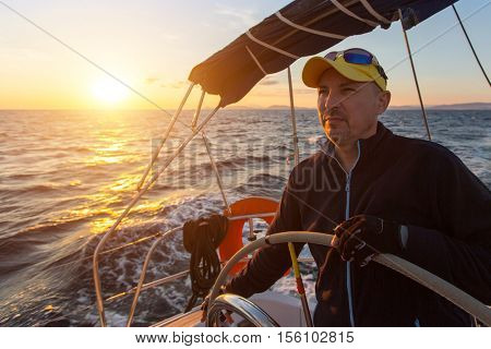 A man controls a sailing ship at sunset. Luxery yacht boat.  