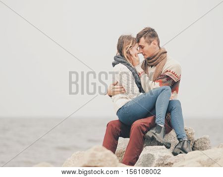 Young attractive couple in knitted sweaters on a cliff on sea shore hugging and holding hands creative toning