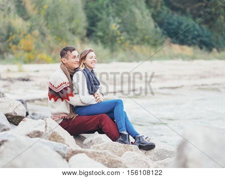 Young attractive couple in knitted sweaters on a cliff on sea shore hugging and holding hands creative toning