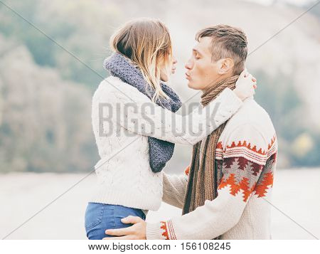 Young attractive couple in knitted sweaters on a cliff on sea shore hugging and kissing creative toning